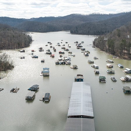 Drone aerial looking north up the cove. Shows full mooring field, covered dock from above, mountains in background. Winter/early spring.