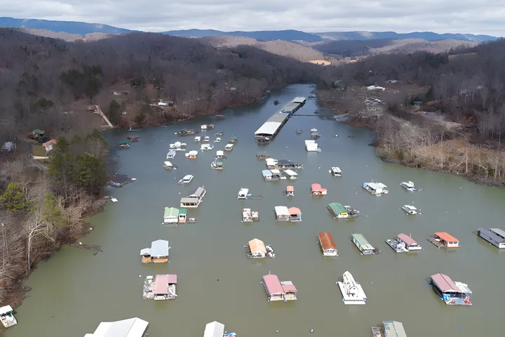 Aerial view of a lake with numerous small docks and floating structures, surrounded by forested hills.