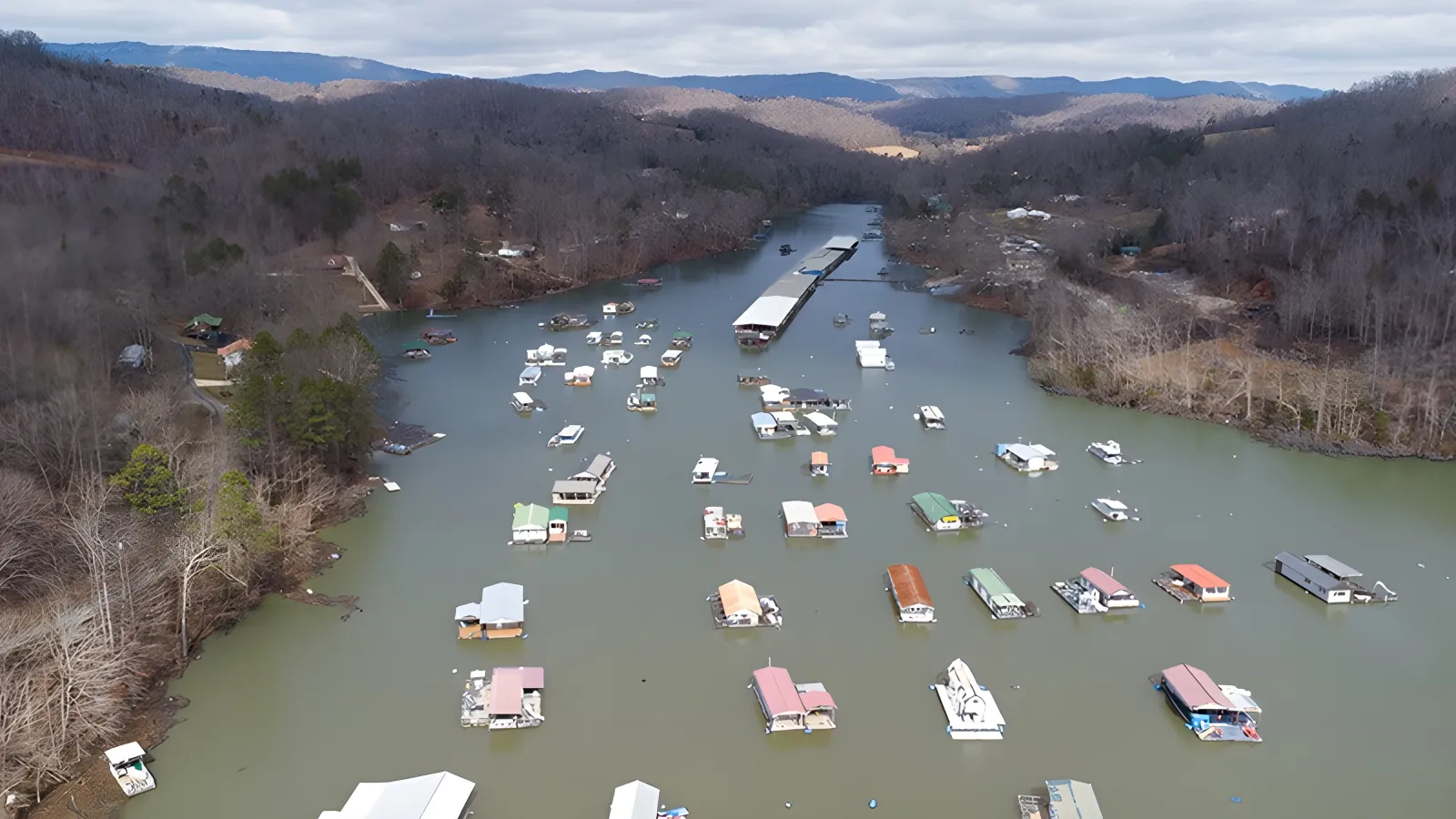 Aerial view of a lake with numerous small docks and floating structures, surrounded by forested hills.
