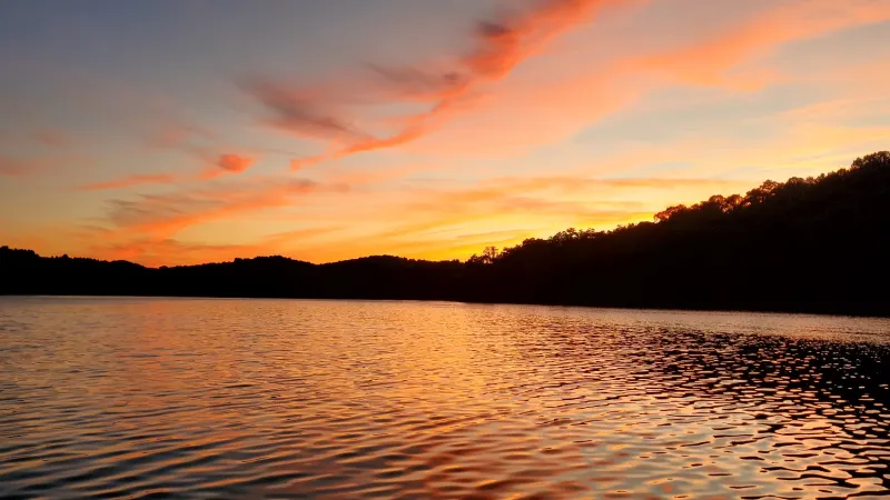 Sunset over a calm lake with orange and pink sky, silhouetted hills in the background.