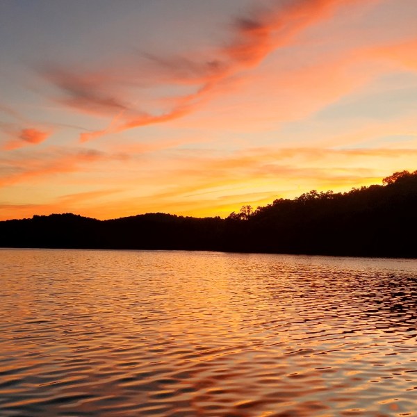 Blue sky with dramatic cloud formations and sun rays over lake. Golden light. Vertical orientation.